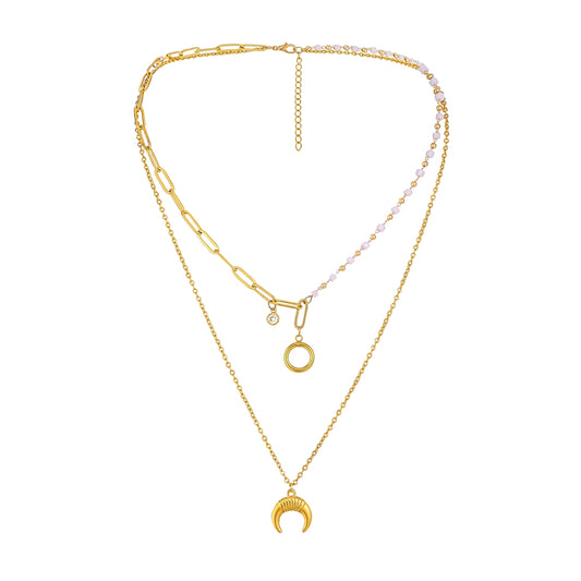 A gold-toned layered necklace set on a plain white background. The necklace features a paperclip chain, a delicate chain with a crescent moon pendant, a small open circle pendant, and a beaded section with pale pink faceted beads.