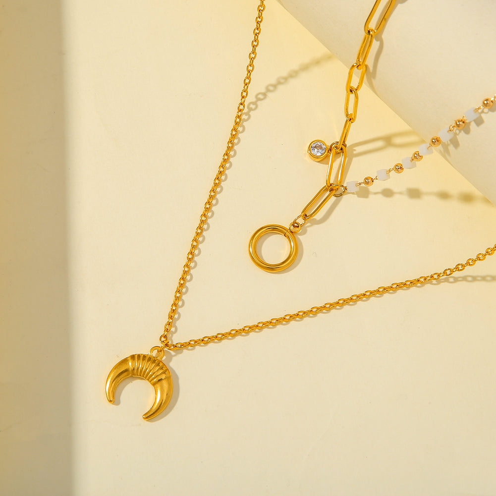 Gold necklaces with moon and circle pendants on a beige background
