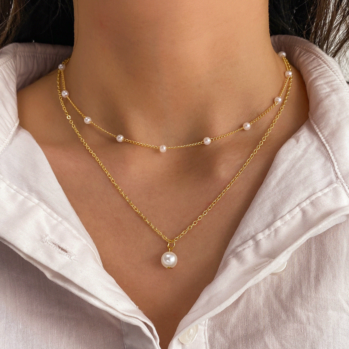 Gold necklace with pearls worn by a person against a neutral background